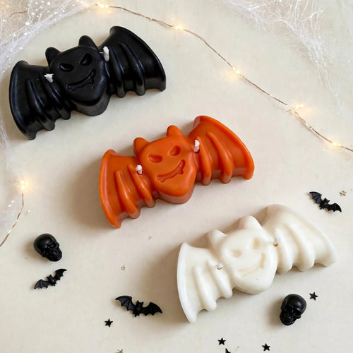 Nox Trio handmade Halloween candle set by Glowbaltic, three hand-poured rapeseed wax bat candles in black, orange and white with two wicks each, among cobwebs, fairy lights and small bats