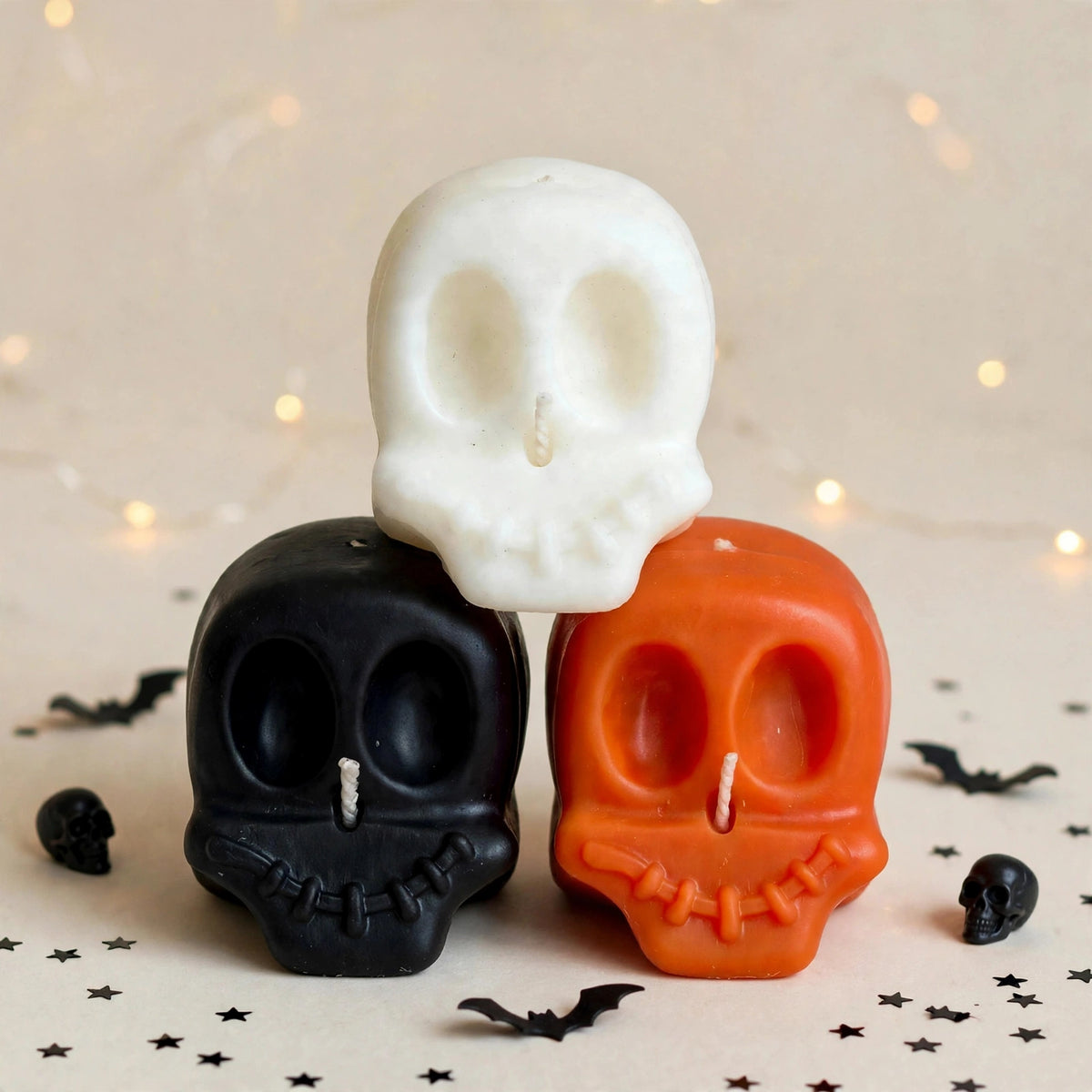 Yorick Trio handmade Halloween candle set by Glowbaltic, three hand-poured rapeseed wax skull candles in black, white and orange, stacked among bats and stars